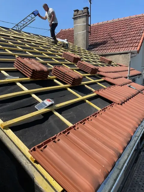 Couvreur en train de poser des tuiles terre cuite sur liteaux et écran sous-toiture lors d’un chantier de rénovation de toiture en Île-de-France